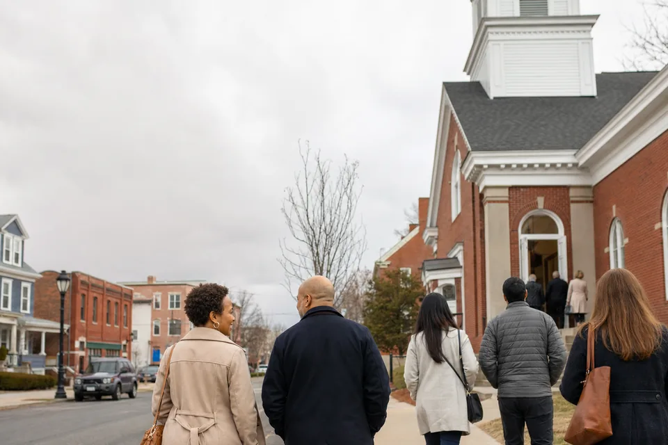 Illustrative overcast New England streetscape with people approaching a neighborhood church.